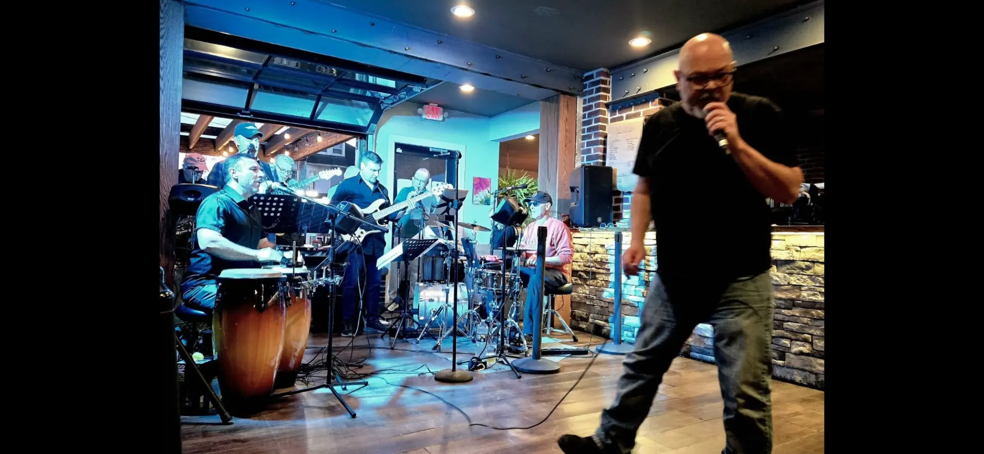A singer walking the floor with a microphone while the band plays behind him in a tavern