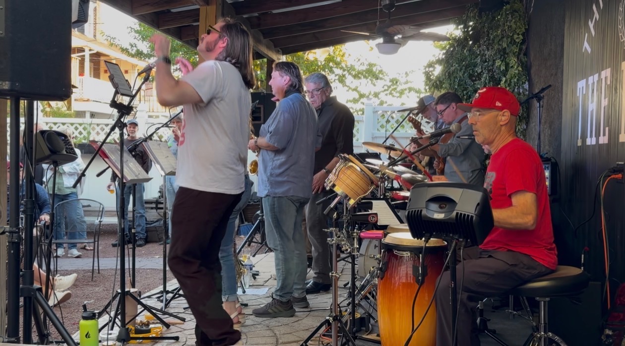 The band playing an outdoor patio show with congas and a singer up front
