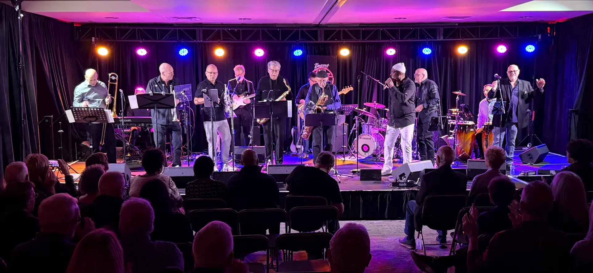 The full 12-piece band on a large stage in front of a seated audience