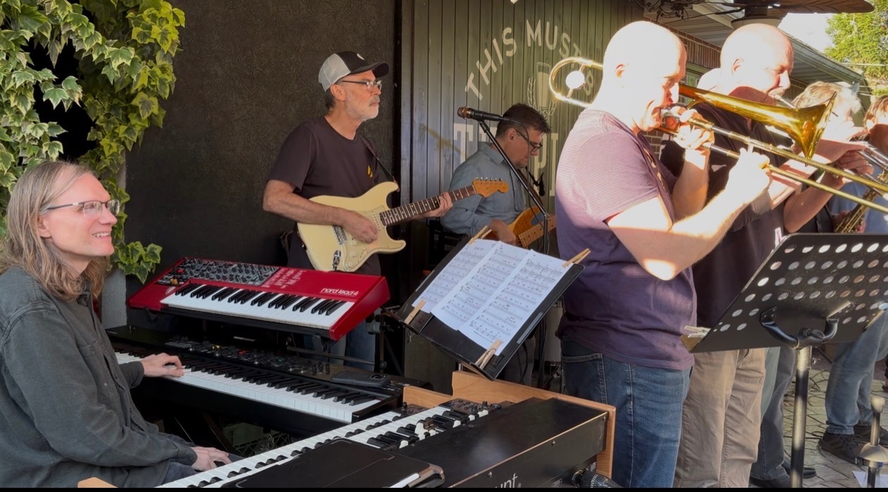 Keyboards, guitar and the trombone section during a daytime outdoor set