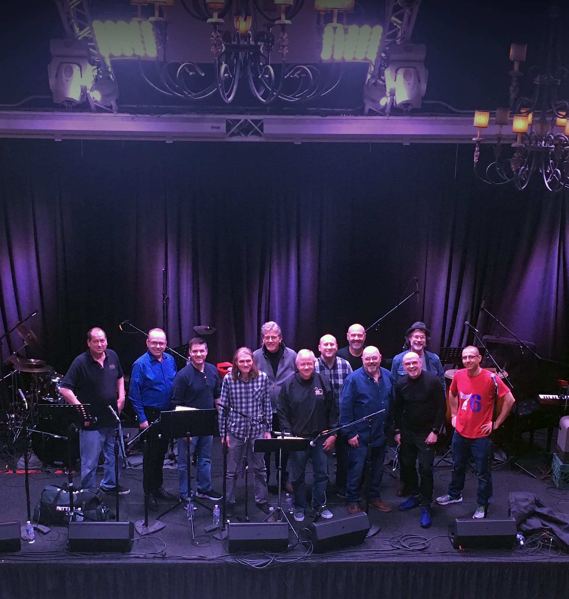 The band posed on stage seen from the balcony, chandeliers overhead